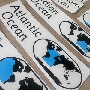 May include: Five white stickers with black text and a blue and black world map illustration. The stickers are labelled "Arctic Ocean", "Southern Ocean", "Indian Ocean", "Atlantic Ocean", and "Ocean".