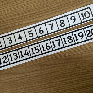 May include: Two white strips of paper with black numbers from 1 to 20. The numbers are in individual boxes on the strips.