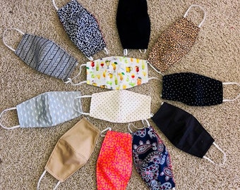 May include: A collection of 10 different fabric face masks with various patterns and colors, including black, white, gray, brown, pink, blue, and green. The masks are all made of cotton fabric and have elastic ear loops.