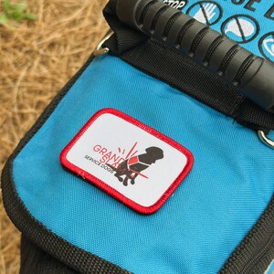 May include: Blue service dog vest with black trim and a black handle. The vest has a patch that says "Grand Slam Service Dogs" with a red border and a graphic of a dog wearing a service vest.