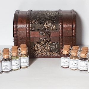 May include: A wooden treasure chest with a floral design and a brass latch, open to reveal 12 small glass jars filled with dried herbs and spices. Each jar has a cork lid and a label with the name of the herb or spice and the text "1/2".