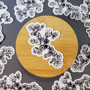 May include: A set of 10 black and white stickers featuring a stylized floral design. The stickers are on a gray surface with a wooden coaster in the center.