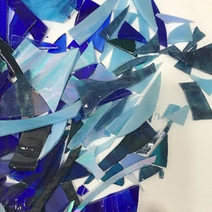 Op de afbeelding: Een stapel blauwe en iriserende glasscherven, perfect voor knutsel- of moza&iuml;ekprojecten.