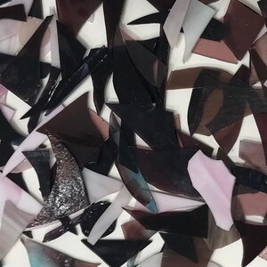 May include: A collection of small, irregular pieces of glass in shades of black, purple, and white. The glass pieces are scattered on a white surface.