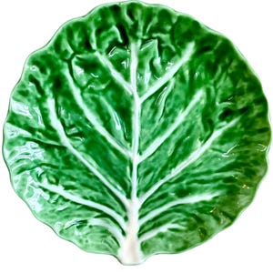 May include: A ceramic plate in the shape of a cabbage leaf. The plate is a vivid green with white veining and a glossy finish. It is designed as a decorative item for serving food.