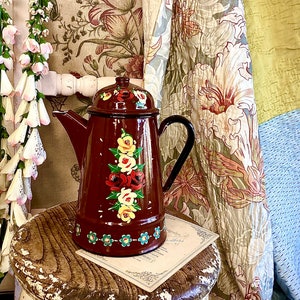 May include: A brown enamel teapot with a black handle and floral painted design. The teapot is sitting on a wooden stool with a white base.