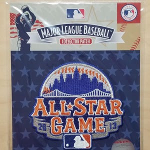 Może przedstawiać: Kolekcjonerska naszywka Major League Baseball z logo All-Star Game 2013. Naszywka ma niebiesko-pomarańczową kolorystykę z motywem miejskim. Opakowanie zawiera logo MLB i piłkę do baseballu.