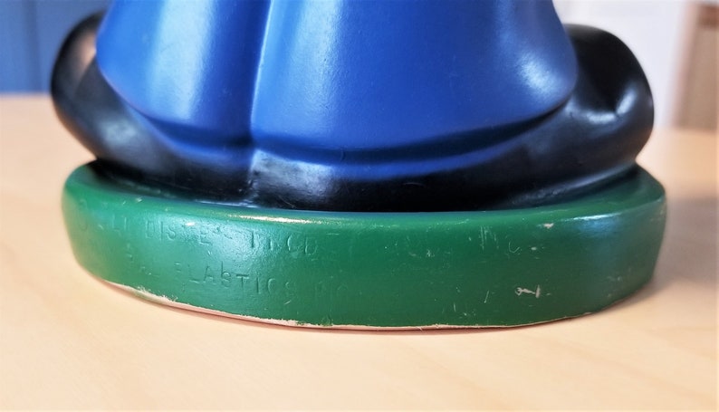 May include: A vintage figurine with a blue top, black accents, and a green base. The base has embossed text that reads "Walt Disney Inc." and "Ideal Plastics Corp."