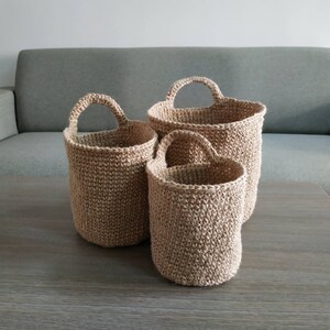 May include: Three woven baskets of varying sizes with handles. The baskets are made of natural fiber and have a light brown color.