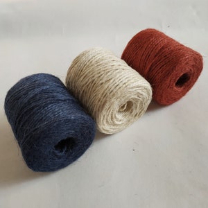 May include: Three spools of twine in different colors: navy blue, natural beige, and rust orange. The spools are made of natural fiber and are perfect for crafting projects.