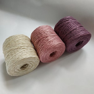 May include: Three spools of twine in different shades of pink and beige. The twine is natural and has a rustic look.