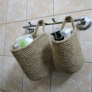 May include: Two beige crocheted hanging baskets with a silver metal rack attached to a tiled wall. The baskets are filled with toiletries, including bottles and tubes.