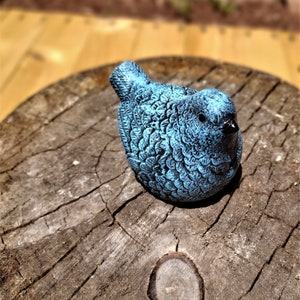May include: A blue bird figurine with a textured surface, sitting on a weathered tree stump.