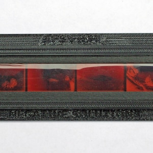 Puede incluir: Un marco negro con una tira de película en su interior. La película es roja y muestra una serie de imágenes. El texto "HIGH GRADE" está impreso en la parte inferior del marco.