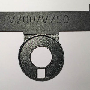 May include: A black plastic 3D printed adapter with a round opening and a rectangular cutout. The adapter is labelled "V700/V750".