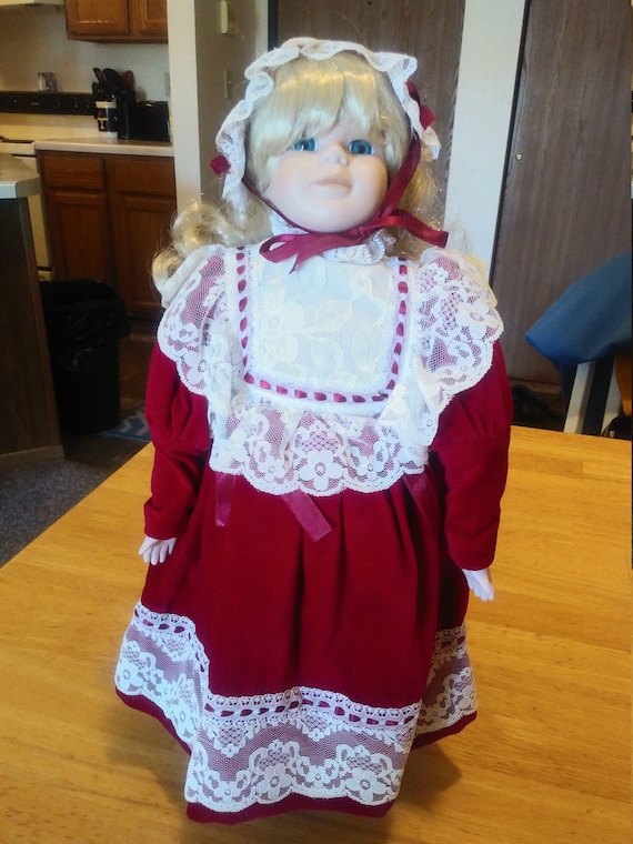Porcelain Doll #112 in red velvet dress with white lace. Circa. 1980s. With metal stand up stand.