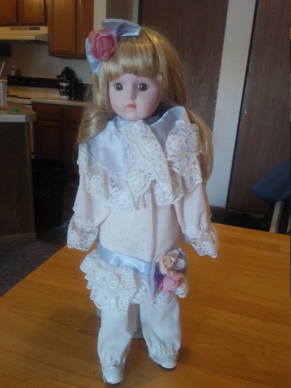 Porcelain Doll #104 in white lace dress with floral bows with metal stand up stand. Circa. 1970s