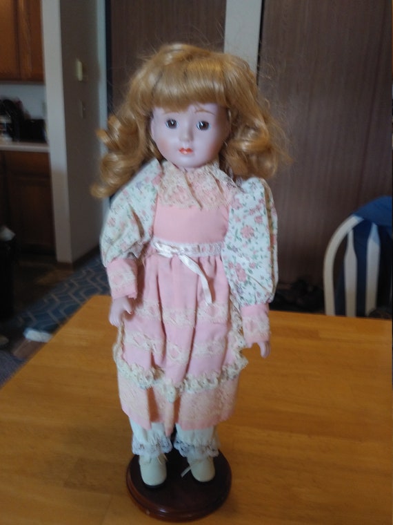 Porcelain Doll #120 with lace, pink and floral outfit. Circa. 1980s with wooden and metal stand up stand.