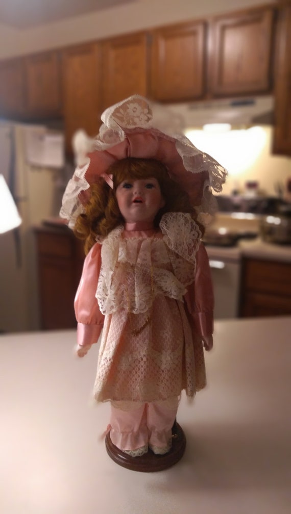 Porcelain doll # 12 with tear drop and pink dress with white lace over the top of dress. With big pink bonnet. Circa. 1980s.