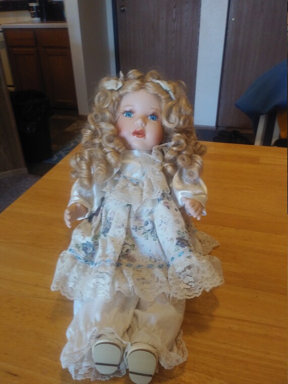 Porcelain Doll #107 with curly hair and a blue floral and lace dress. Circa. 1980s