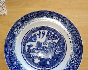 Może przedstawiać: Niebieski i biały talerz porcelanowy z tradycyjnym wzorem wierzby. Talerz przedstawia centralny obraz wierzby płaczącej, mostu, łodzi i ptaków. Brzeg talerza jest ozdobiony powtarzającym się wzorem geometrycznych kształtów.