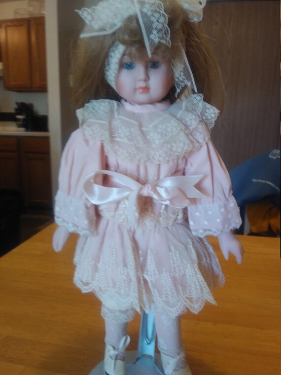 Porcelain Doll # 108 with pink dress ornate lace that comes with metal stand up stand. Circa. 1970s