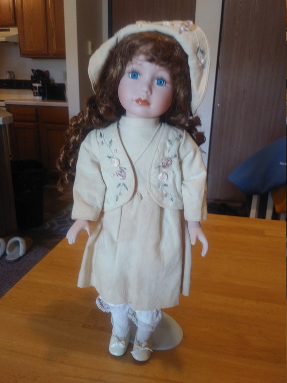 Porcelain Doll # 115 with bonnet and purse in nice floral engraved outfit. Circa. 1980s with metal stand up stand.