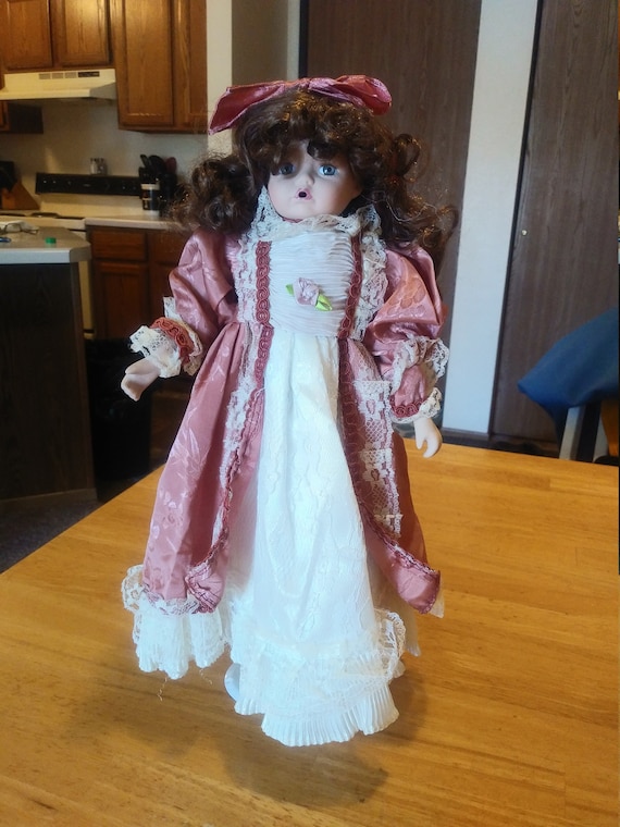 Porcelain Doll # 111 with pink satin dress with white lace. Circa. 1980s with metal stand up stand.