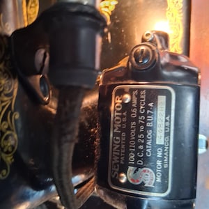 May include: Close-up of a black sewing machine motor with the text "SEWING MOTOR" and technical specifications. The motor is labeled "PATENTED U.S.A." and includes voltage and cycle details. The motor is attached to a vintage sewing machine.
