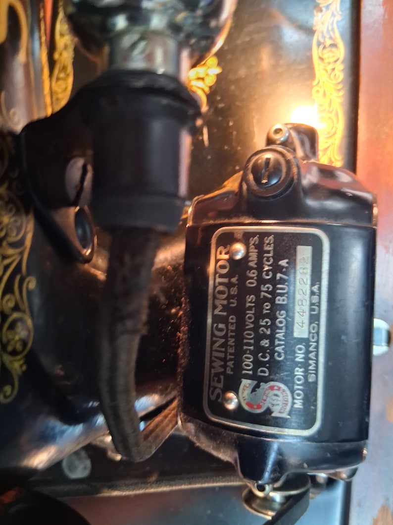 May include: Close-up of a black sewing machine motor with the text "SEWING MOTOR" and technical specifications. The motor is labeled "PATENTED U.S.A." and includes voltage and cycle details. The motor is attached to a vintage sewing machine.