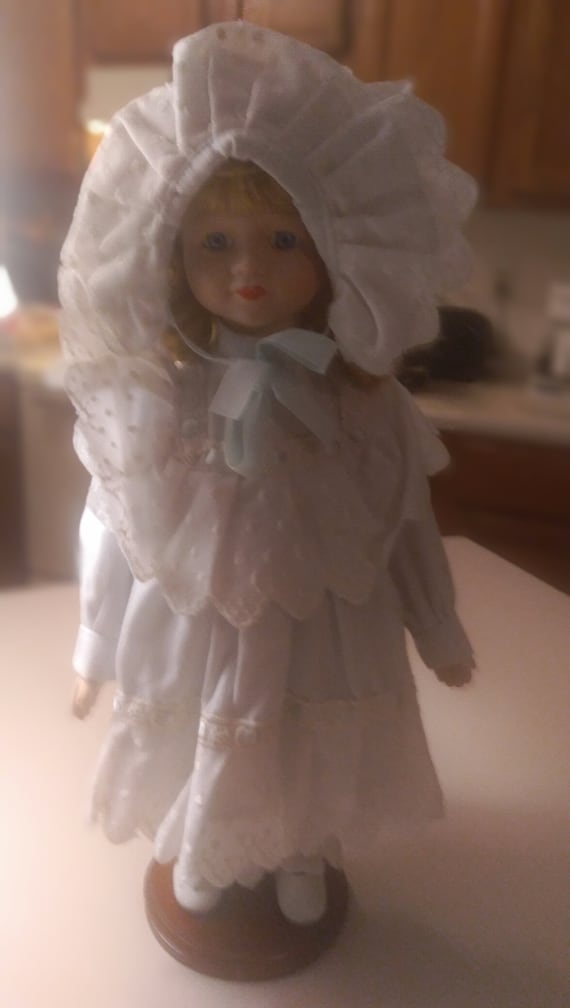 Porcelain doll # 10 freckle face girl in a blue bonnet and a blue and white dress circa. 1980s with stand included.