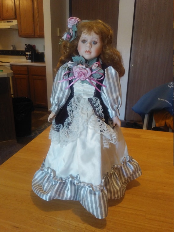 Porcelain Doll # 110 with a silver, black and white lace dress with a pink flower centerpiece circa. 1980s with metal stand up stand