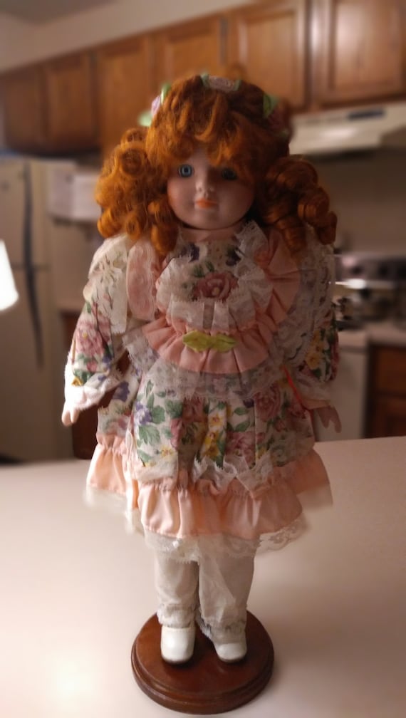 Porcelain doll # 15 flower pattern dress with white lace and pink and green bows in her hair. Circa. 1980s