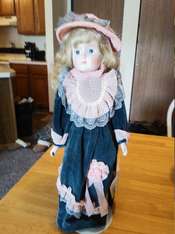 Porcelain Doll #129 in a Blue Velvet dress with an Orange hat and orange lace. Circa.1980s with metal stand up stand.