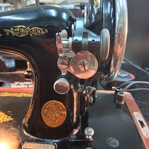May include: Close-up of a vintage black Singer sewing machine with gold floral detailing. The machine features a large hand wheel, various dials, and a Singer emblem. The serial number 50318463 is visible on the base.