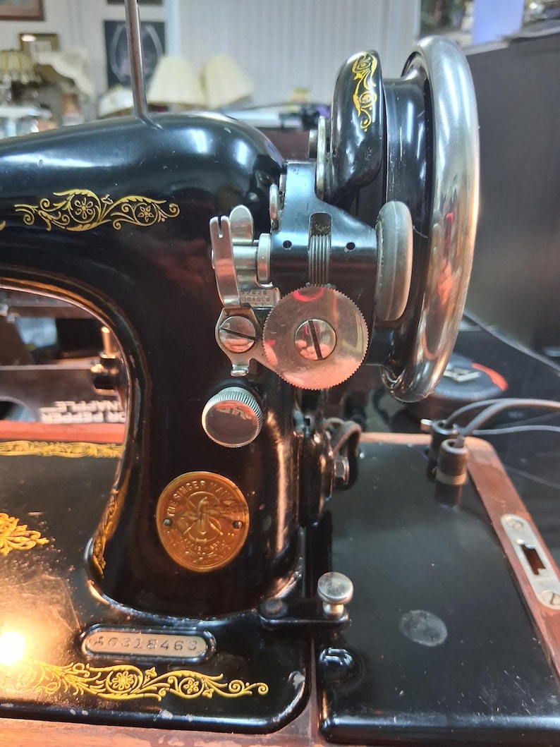 May include: Close-up of a vintage black Singer sewing machine with gold floral detailing. The machine features a large hand wheel, various dials, and a Singer emblem. The serial number 50318463 is visible on the base.