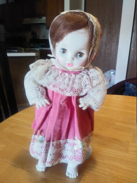 Vintage doll Circa. 1970s with pink little red riding hood style dress and lace. Comes with stand.