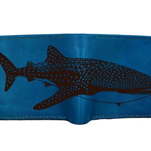 May include: A blue leather wallet with a brown whale shark illustration. The whale shark has a dotted pattern. The wallet has a stitched border. The design is a detailed depiction of the sea creature.