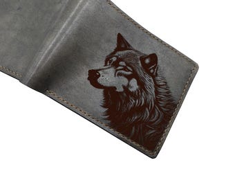 May include: Gray leather wallet with a detailed wolf portrait etched on the front. The wallet is open, revealing the interior. The edges are stitched with a contrasting thread, and the overall design is minimalist and rugged.