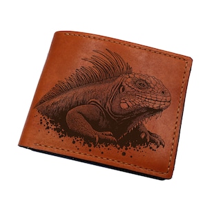 Puede incluir: Una cartera de cuero marrón con un grabado detallado de una iguana. La iguana está representada en un estilo artístico detallado, con escamas y espinas visibles. La cartera tiene un diseño clásico de dos pliegues.