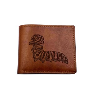 Pode incluir: Carteira de couro castanho com um design de lagarta gravado. A carteira é retangular e tem uma borda costurada. A lagarta é de cor castanha escura e está centrada na frente.