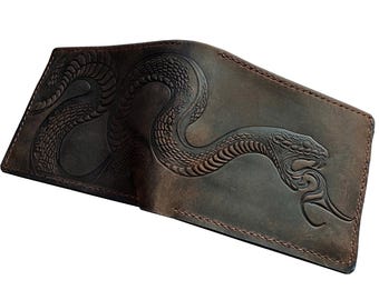 Peut inclure: Un portefeuille en cuir marron avec un motif de serpent en relief. Le serpent est enroulé et a une tête détaillée.