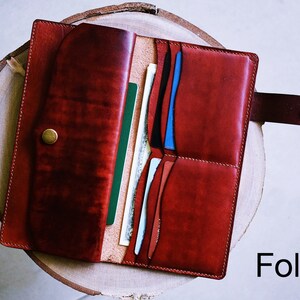 May include: A red leather wallet with multiple card slots and a snap closure. The wallet is open and shows several cards and bills inside. The word "Folder" is printed in white on a black background below the wallet.