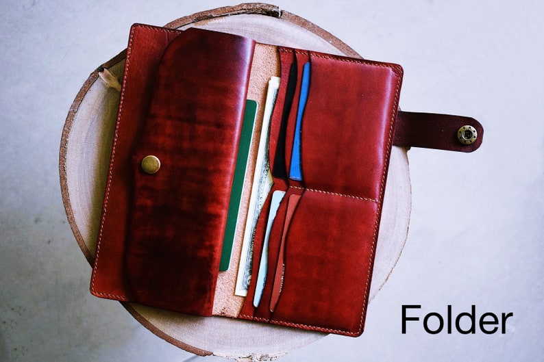 May include: A red leather wallet with multiple card slots and a snap closure. The wallet is open and shows several cards and bills inside. The word "Folder" is printed in white on a black background below the wallet.