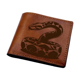 Könnte beinhalten: Ein braunes Leder-Brieftaschen-Faltmodell mit einer dunkelbraunen Gravur einer zusammengerollten Schlange auf der Vorderseite. Die Brieftasche weist sichtbare Nähte entlang der Kanten und eine glatte Oberfläche auf dem äußeren Ledermaterial auf.