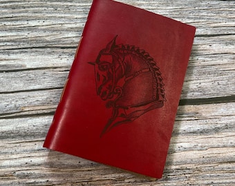 May include: A red leather journal with a detailed illustration of a horse's head in profile, embossed on the front cover.