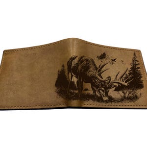 Può includere: Portafoglio aperto in pelle marrone chiaro con un'immagine incisa dettagliata di un cervo con grandi corna, ambientato in una scena forestale. Il portafoglio è aperto, mostrando il design interno e le cuciture.