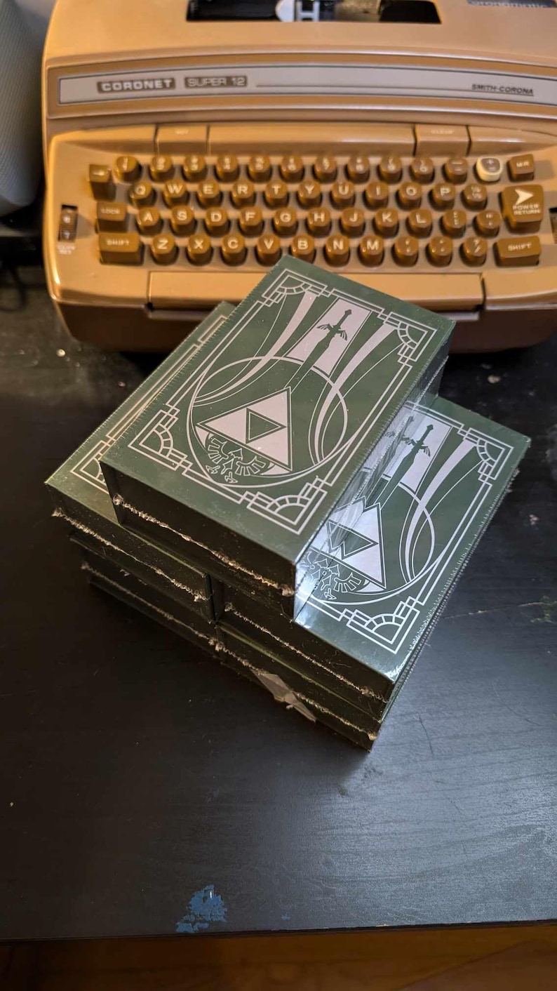 May include: A stack of green cardboard boxes with a white design featuring a stylized triangle and swords. The boxes have a decorative border.
