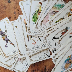 May include: A spread of tarot cards with illustrations of people and symbols. The cards are white with gold trim and feature a variety of suits, including wands, swords, and cups. The cards are arranged in a fan shape, with the top card showing a knight riding a horse.