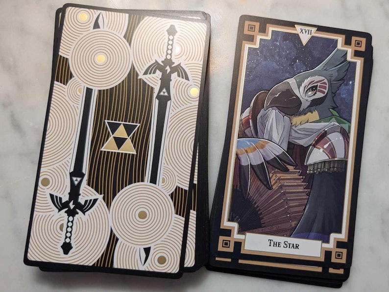 May include: Two tarot cards, one with a black and gold design featuring a sword and the other with a black and gold frame and a colorful illustration of a bird with a star in the corner and the text "The Star".